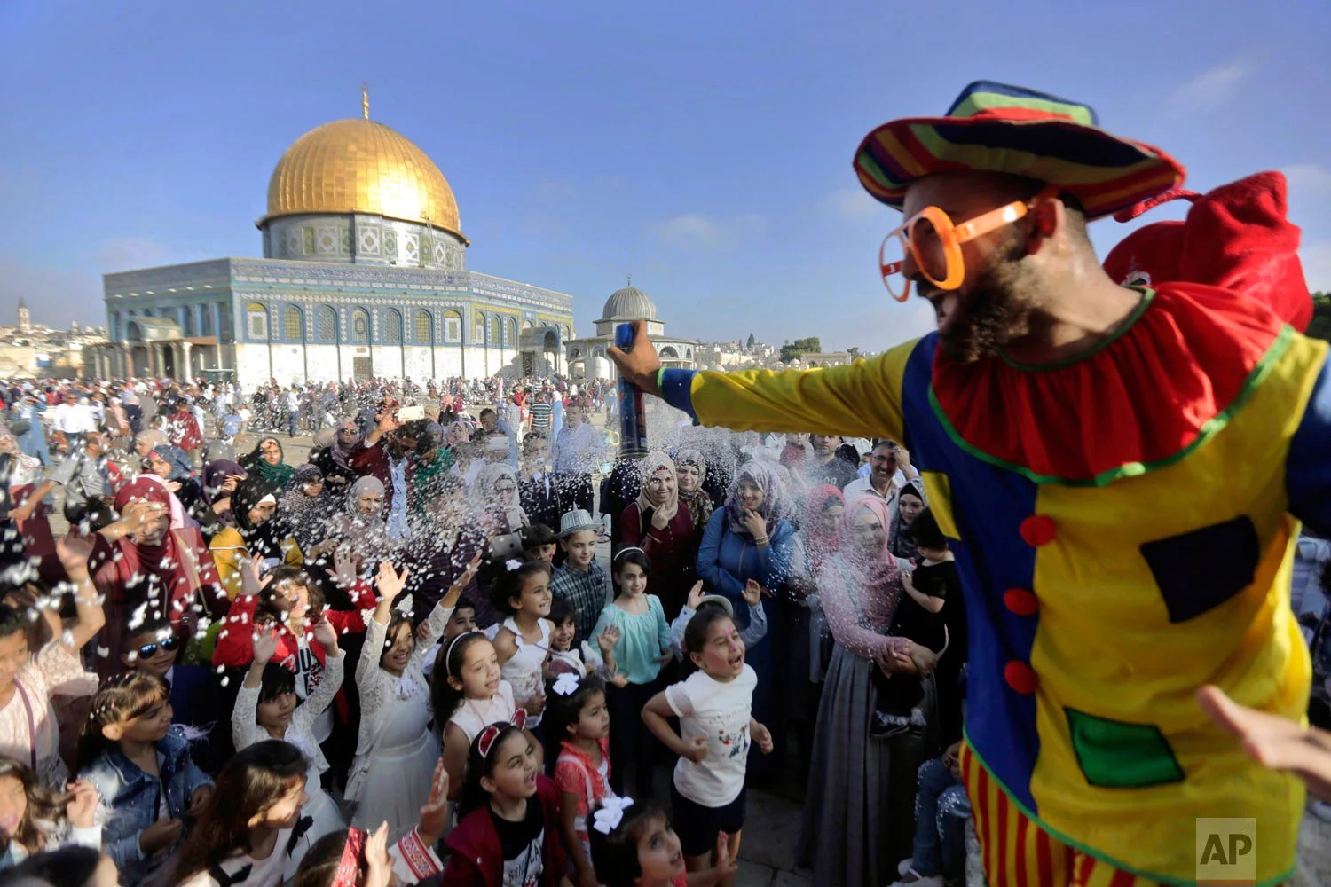A clown sprays foam towards a group of children on the first day of Eid al-Adha near the Dome of the Rock Mosque in the Al Aqsa Mosque compound in Jerusalem's old city, Tuesday, Aug. 21, 2018. During the Eid al-Adha, or Feast of Sacrifice, Muslims slaughter sheep or cattle to distribute portions of the meat to the poor. (AP Photo/Mahmoud Illean)