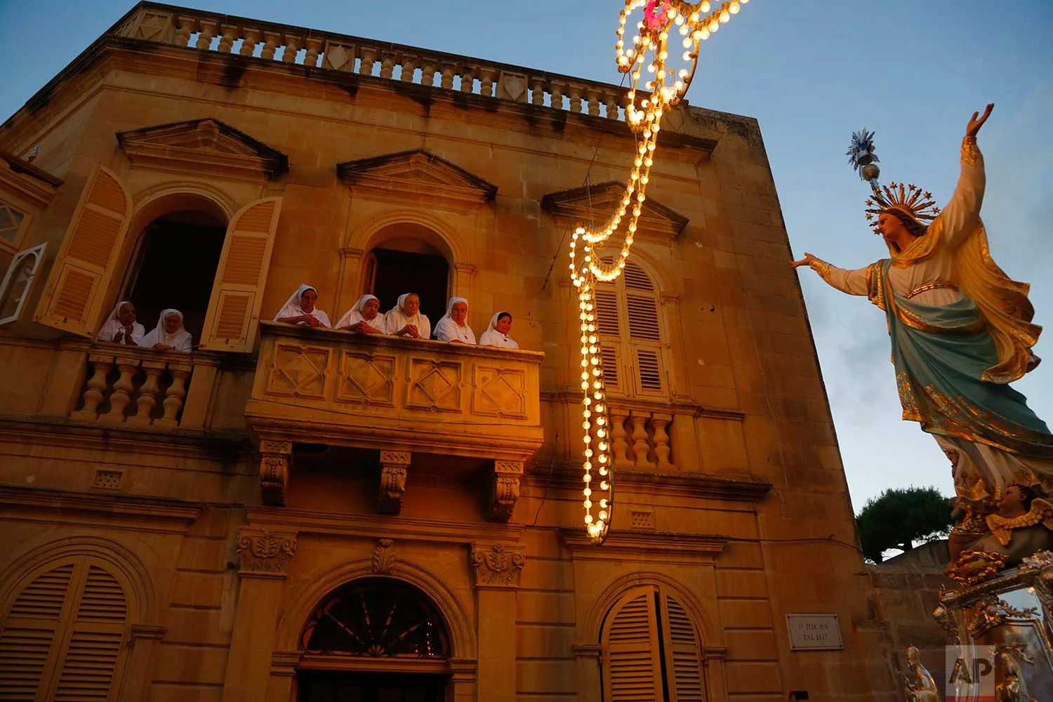 In this photo taken on Wednesday, Aug. 15, 2018, nuns watch the statue of the Virgin Mary being carried through the streets of Rabat on the island of Gozo in the Maltese archipelago, during the feast day of the Assumption of Mary. (AP Photo/Niranjan Shrestha)