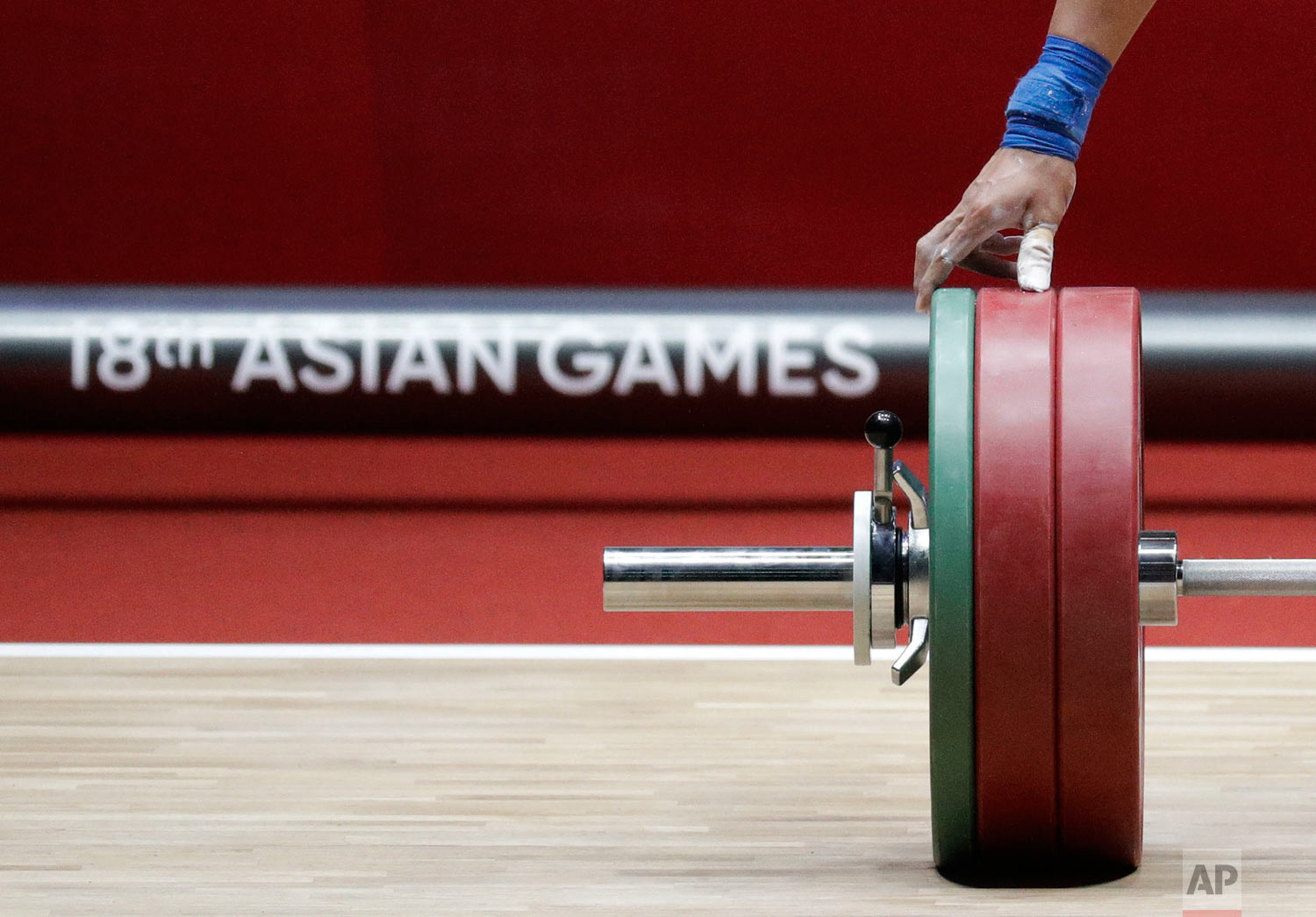 Indonesia's Wijo Bin inspects the weights on the bar as he competes in the men's 56kg weightlifting at the 18th Asian Games in Jakarta, Indonesia on Monday, Aug. 20, 2018. (AP Photo/Aaron Favila)