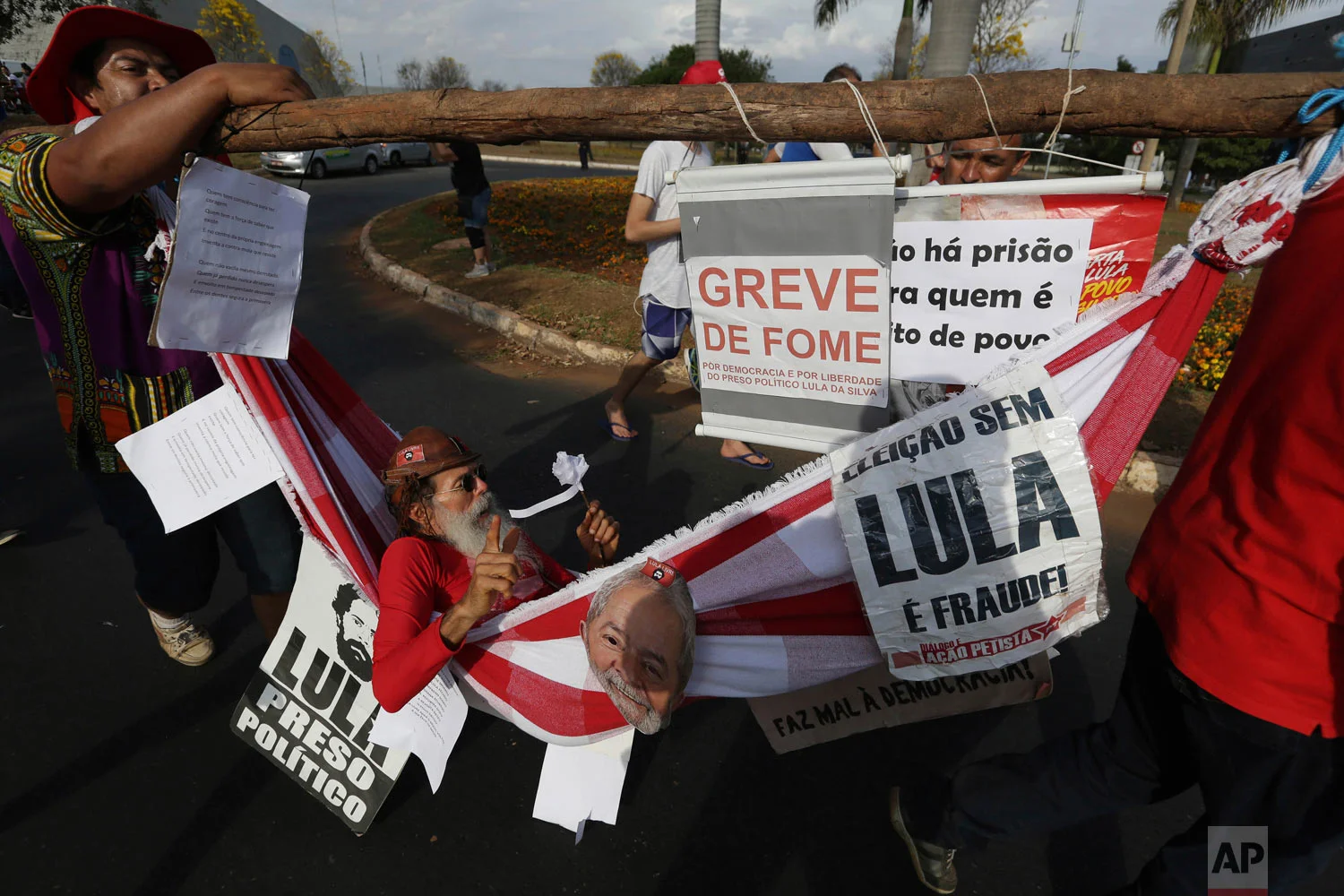A supporter of Brazil's jailed, former President Luiz Inacio Lula da Silva is carried in a hammock while he is on hunger strike to protest the former leader's corruption conviction, during a march in Brasilia, Brazil, Aug. 15 2018. The Workers' Party registered da Silva as its candidate for president Wednesday, attempting to muscle him into the race to lead Latin America's largest nation and forcing a showdown with Brazilian electoral authorities. (AP Photo/Eraldo Peres)