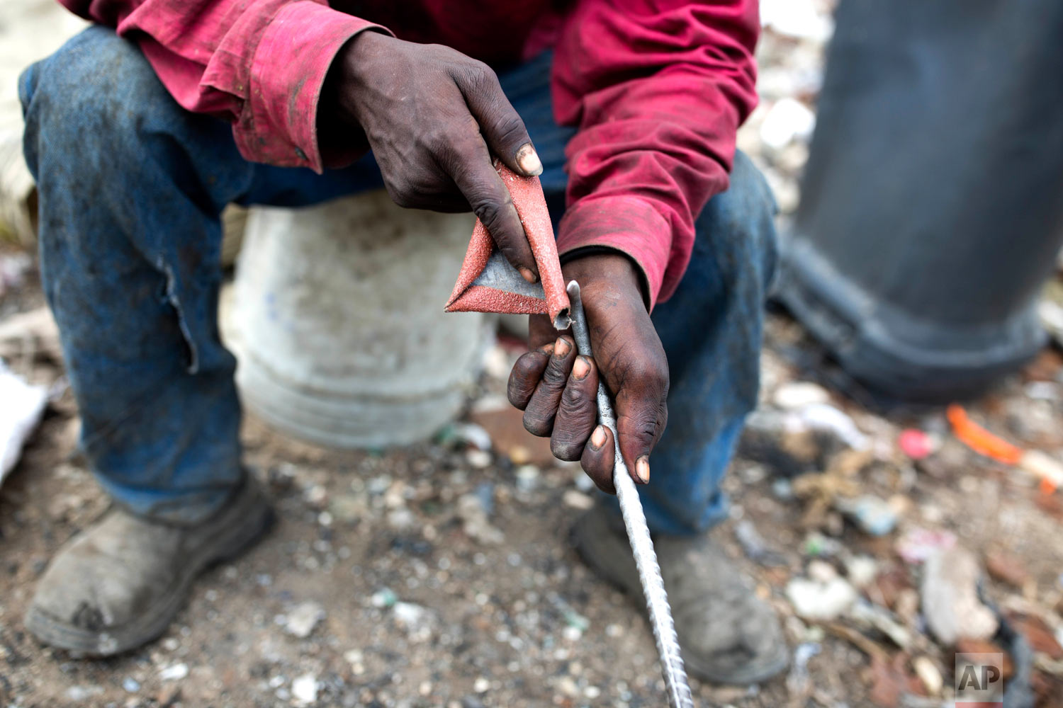  Changlair Aristide sharpens a metal rod he uses to pick through the rubble. Aug. 23, 2018. (AP Photo/Dieu Nalio Chery) 