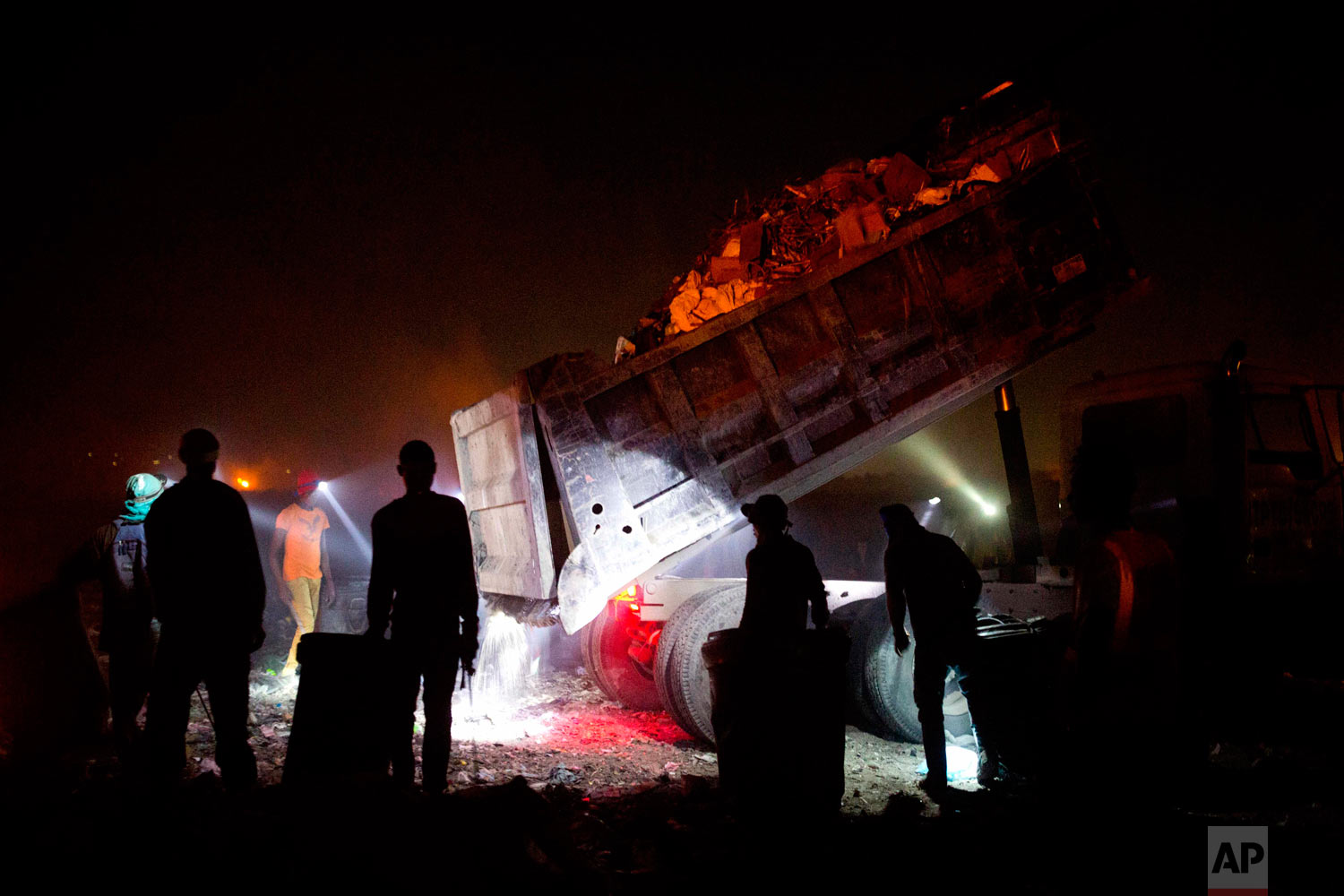  People use headlamps to continue scavenging at night as a truck prepares to dump its load. Aug. 30, 2018. (AP Photo/Dieu Nalio Chery) 