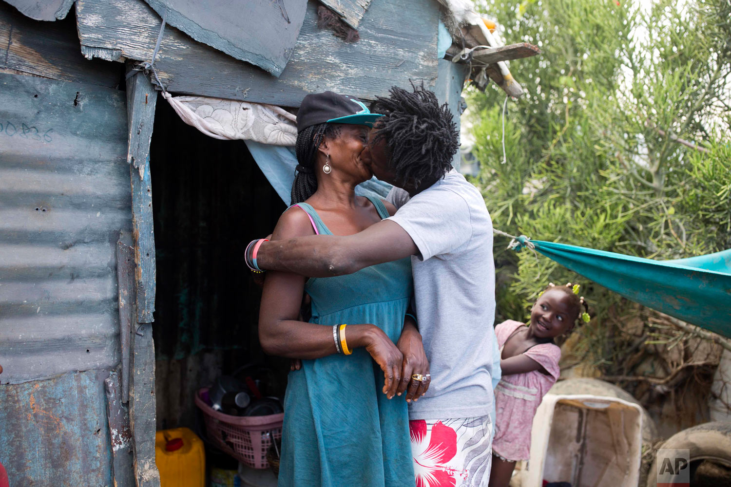  Changlair Aristide kisses his wife Violene Mareus as their daughter Viergeline looks on outside their home.  Mareus cares for their three daughters at home where she sells cigarettes and alcohol. Aug. 25, 2018. (AP Photo/Dieu Nalio Chery) 