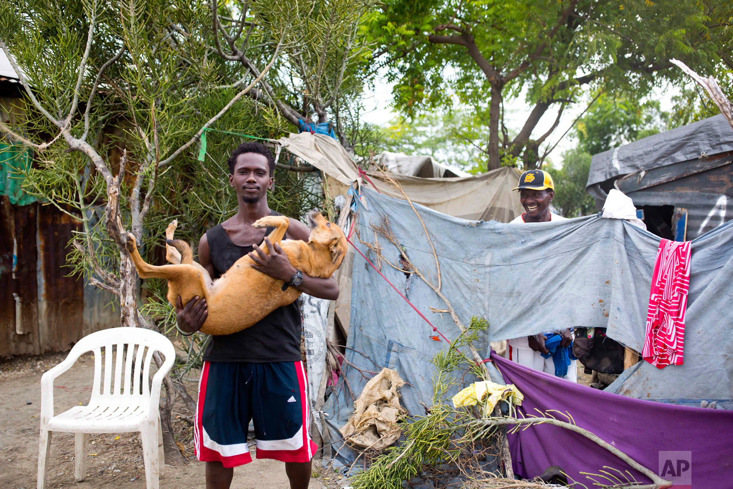  Guerdy Joseph holds his dog outside the home of his friend Changlair Aristide, right, where they live on the edges of the landfill. Aug. 29, 2018. (AP Photo/Dieu Nalio Chery) 