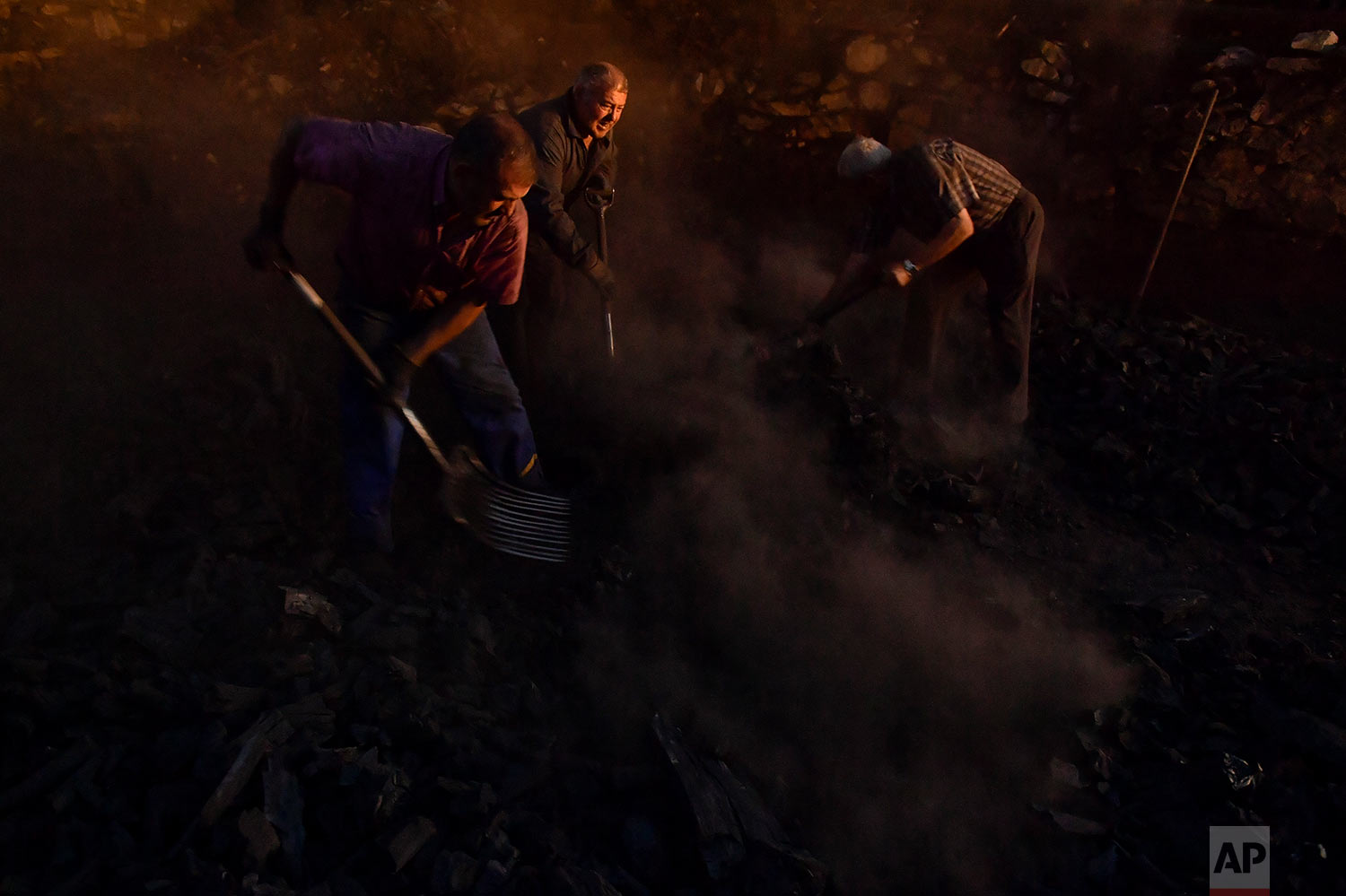  In this Tuesday, Sept.11, 2018 photo, Jesus Luis Remiro, center, picks up charcoal with his brother, Salvador, right, and Jose Mari Nieva, left, as part of a process to produce traditional charcoal in Viloria, northern Spain. (AP Photo/Alvaro Barrie