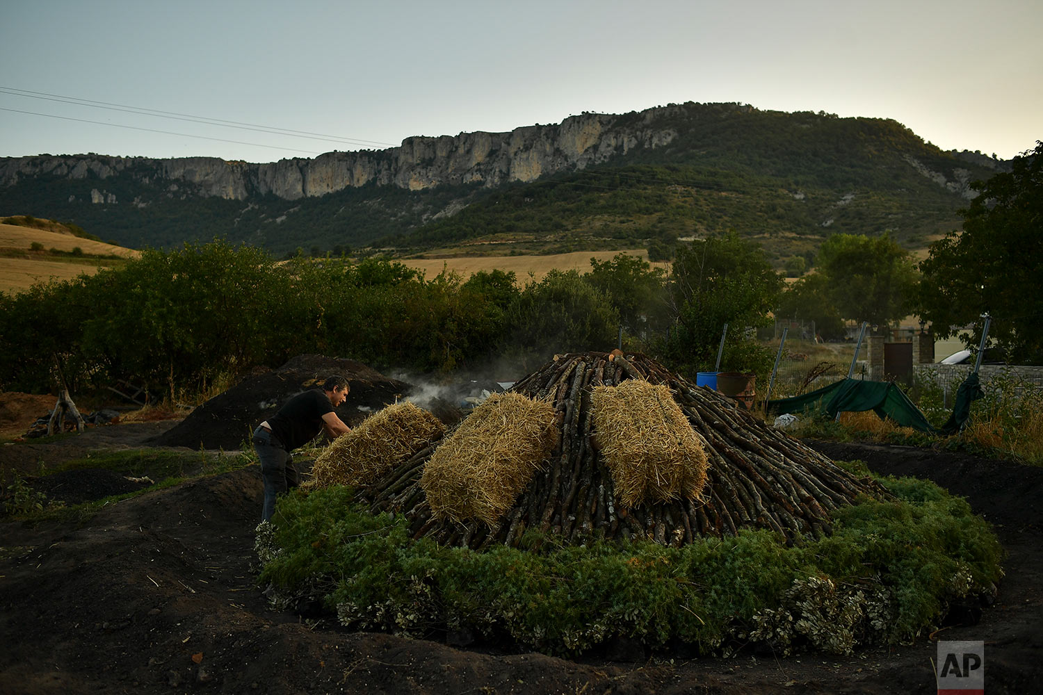  In this Wednesday, Aug. 29, 2018 photo, Miguel Lander, 56, places straw bales on wood piled up as part of the process to produce traditional charcoal, in the town of Viloria, northern Spain. (AP Photo/Alvaro Barrientos) 