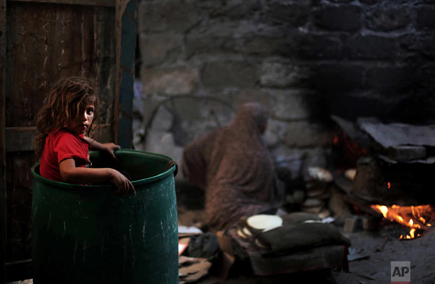  In this June 20, 2016 photo, a Palestinian girl plays in a barrel as her mother bakes bread for a Ramadan dinner at their house in el-Zohor slum, on the outskirts of Khan Younis refugee camp, southern Gaza Strip. (AP Photo/Khalil Hamra) 