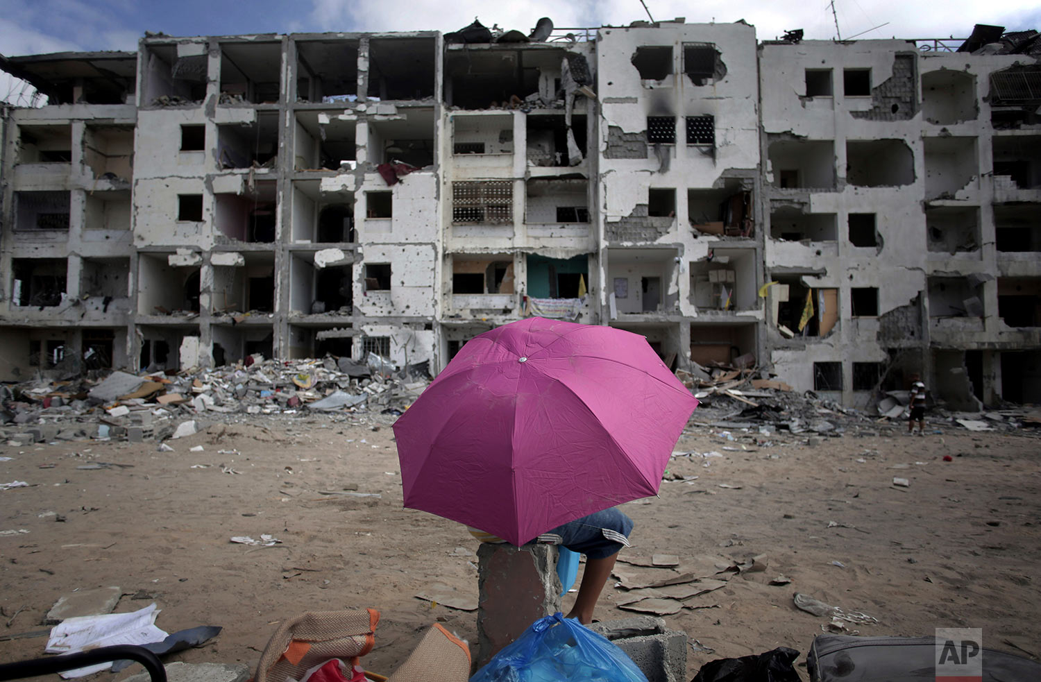  In this Aug. 11, 2014 photo, a Palestinian boy holds an umbrella as he rests in front of the damaged Nada Towers residential neighborhood in the town of Beit Lahiya, northern Gaza Strip. (AP Photo/Khalil Hamra) 