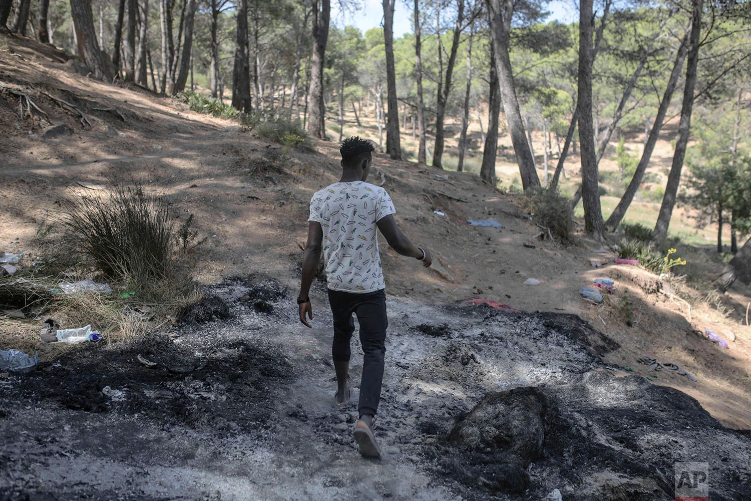 A sub-Saharan migrant aiming to cross to Europe walks on a burnt patch following a raid by police, near Masnana, Sept. 5, 2018, on the outskirts of Tangier, Morocco. (AP Photo/Mosa'ab Elshamy)
