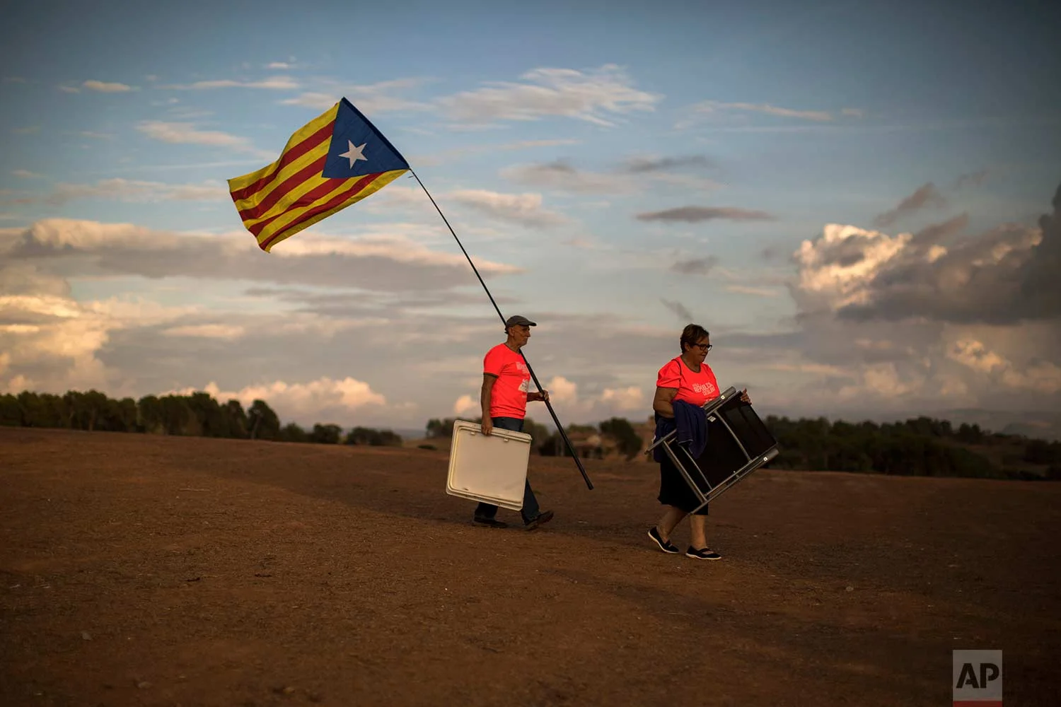 In this Tuesday, Sept. 18, 2018 photo, pro independence people carry chairs and a picnic basket, as they arrive to a field overlooking the Lledoners prison in Sant Joan de Vilatorrada, about 50 kilometres away from Barcelona, Spain. (AP Photo/Emilio Morenatti)