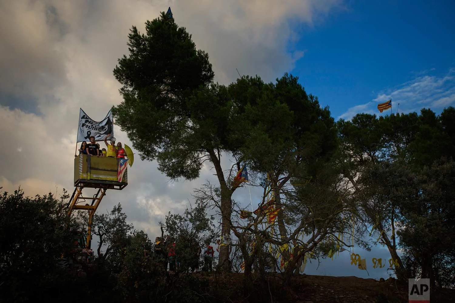 In this Tuesday, Sept. 18, 2018 photo, a tractor lift up pro independence supporters holding a banner for former minister Jordi Turull and chanting "freedom", on a field overlooking the Lledoners prison, in Sant Joan de Vilatorrada, about 50 kilometres away from Barcelona, Spain. (AP Photo/Emilio Morenatti)