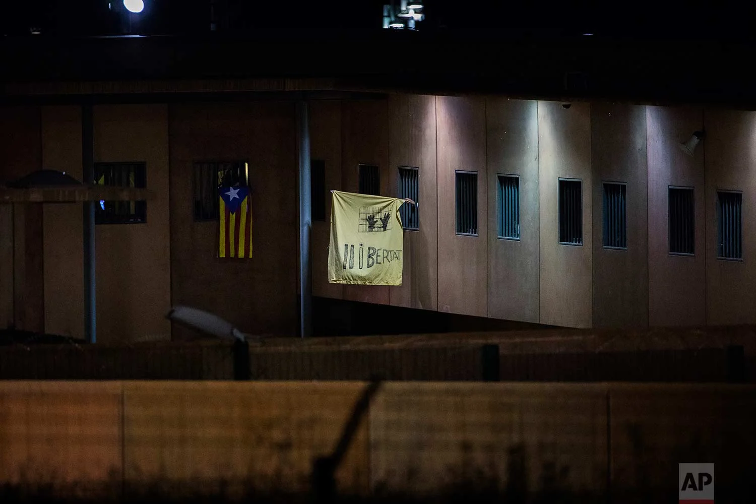 In this Tuesday, Sept. 18, 2018 photo, an "estelada" or independence flag, and a banner reading in Catalan "Freedom", are waved from windows of cells in Lledoners prison, in Sant Joan de Vilatorrada, about 50 kilometres away from Barcelona, Spain. (AP Photo/Emilio Morenatti)