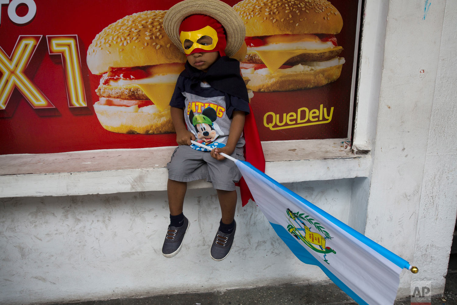  A boy wearing a costume holds a Guatemalan flag as he sits outside a local fast food restaurant waiting with his father for a march against Guatemalan President Jimmy Morales and corruption in Guatemala City, Thursday, Sept. 20, 2018. Thousands marc