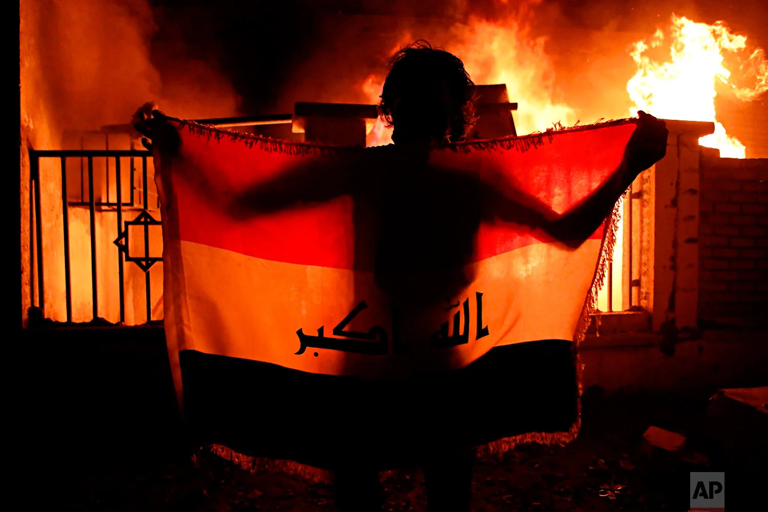 A man holds a national flag while protesters burn the municipal complex during protests demanding better public services and jobs in Basra, 340 miles (550 km) southeast of Baghdad, Iraq, Sept. 5, 2018. (AP Photo/Nabil al-Jurani)