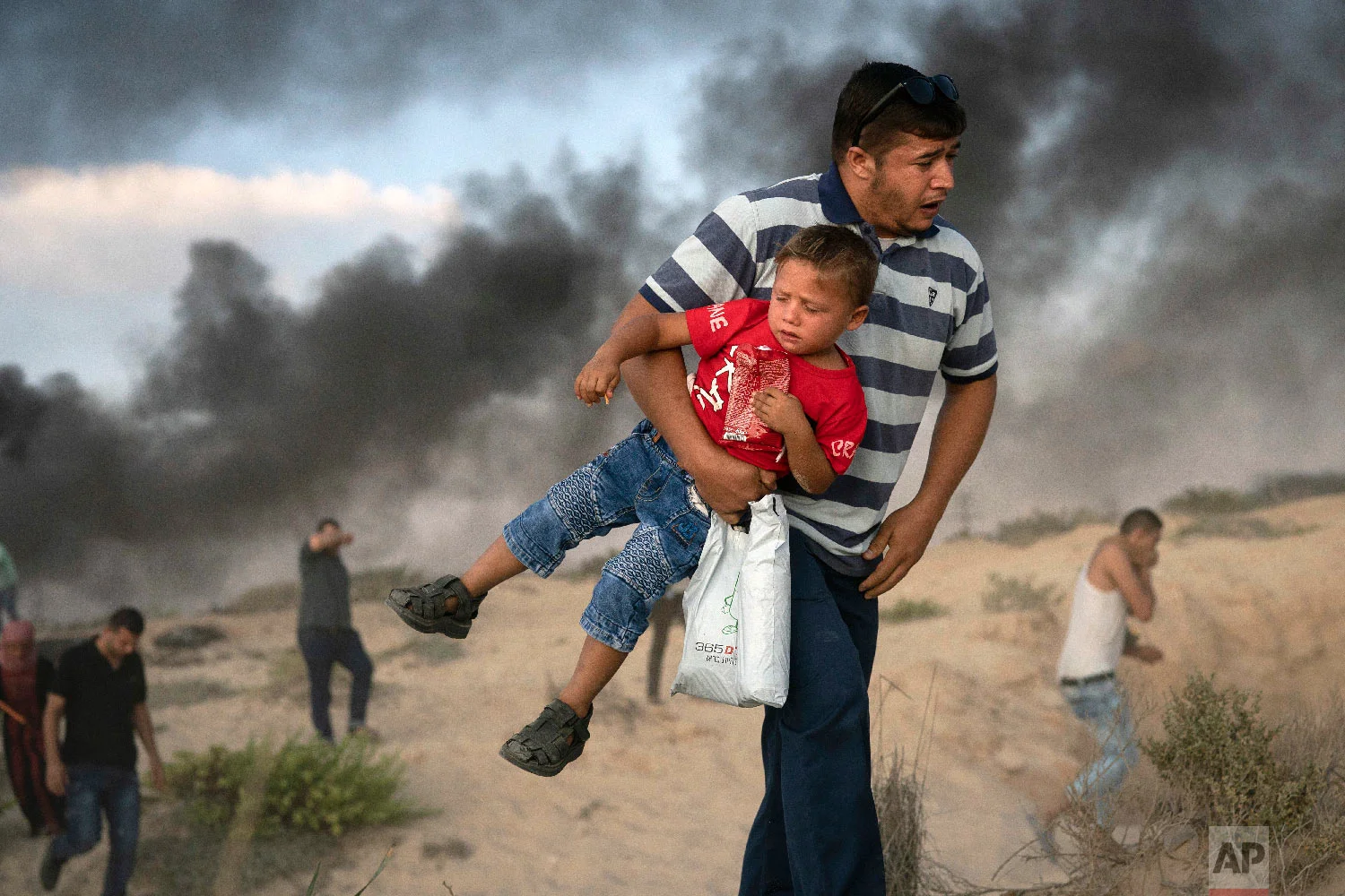A Palestinian protester carries a boy as he runs from tear gas fired by Israeli soldiers during a protest on the beach near the border with Israel in Beit Lahiya, northern Gaza Strip, Monday, Sept. 10, 2018. (AP Photo/Felipe Dana)
