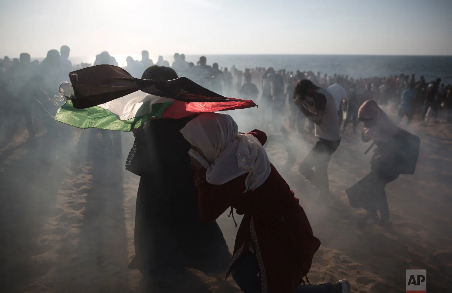 Palestinian protesters run for cover from teargas fired by Israeli soldiers during a protest on the beach at the border with Israel near Beit Lahiya, northern Gaza Strip, Sept. 24, 2018.(AP Photo/Khalil Hamra)