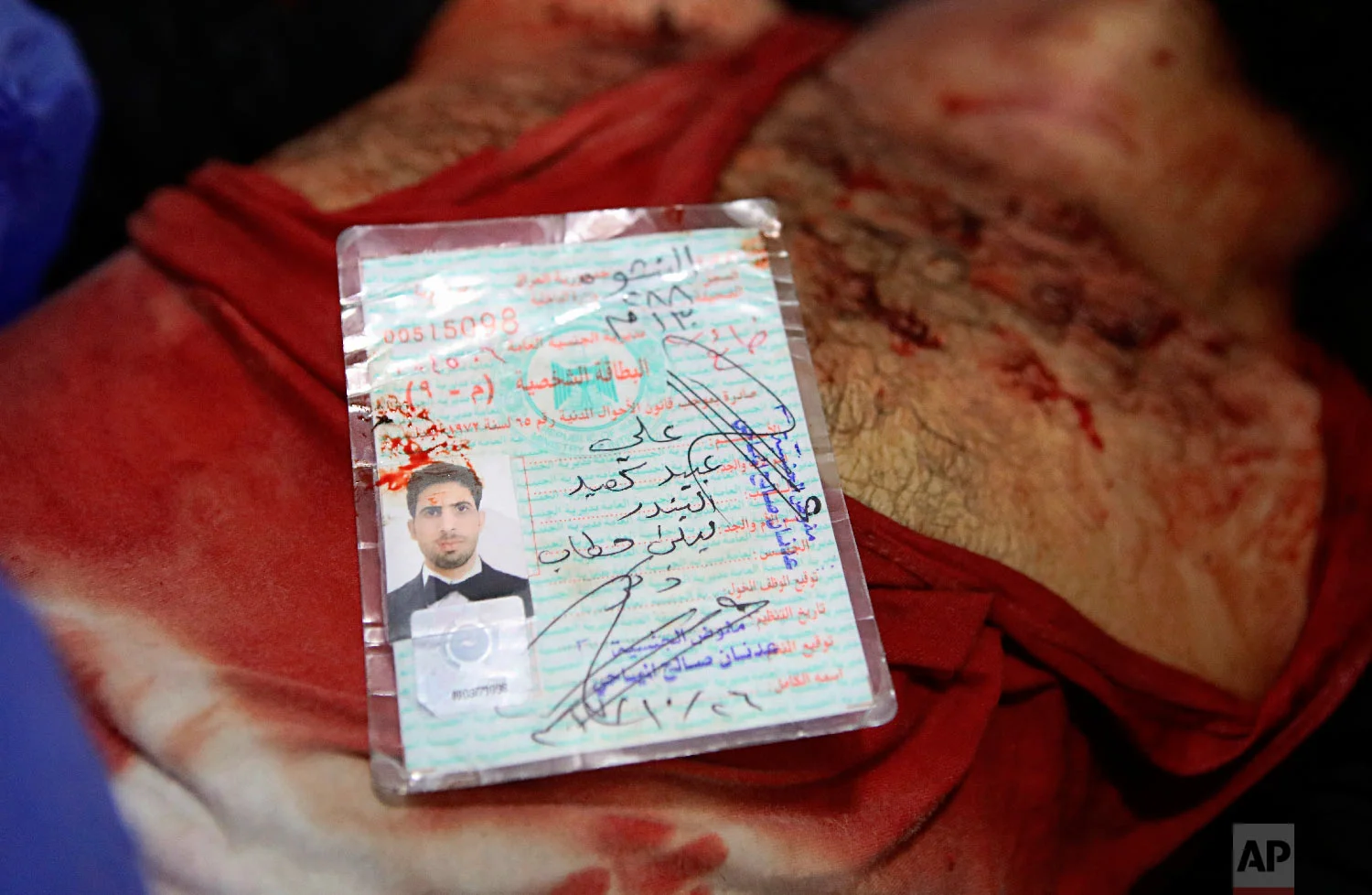 The blood-stained identification card of Ali Obaid, killed during a protest, lies on his body, Tuesday, Sept. 4, 2018, in Basra, 340 miles (550 kilometers) southeast of Baghdad, Iraq.(AP Photo/Nabil al-Jurani)
