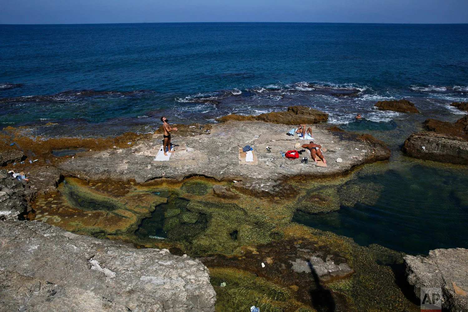 Lebanese men sunbathe on the rocky shore of the Mediterranean Sea off the Corniche, or waterfront promenade, in Beirut, Lebanon, Sept. 26, 2018. (AP Photo/Hussein Malla)