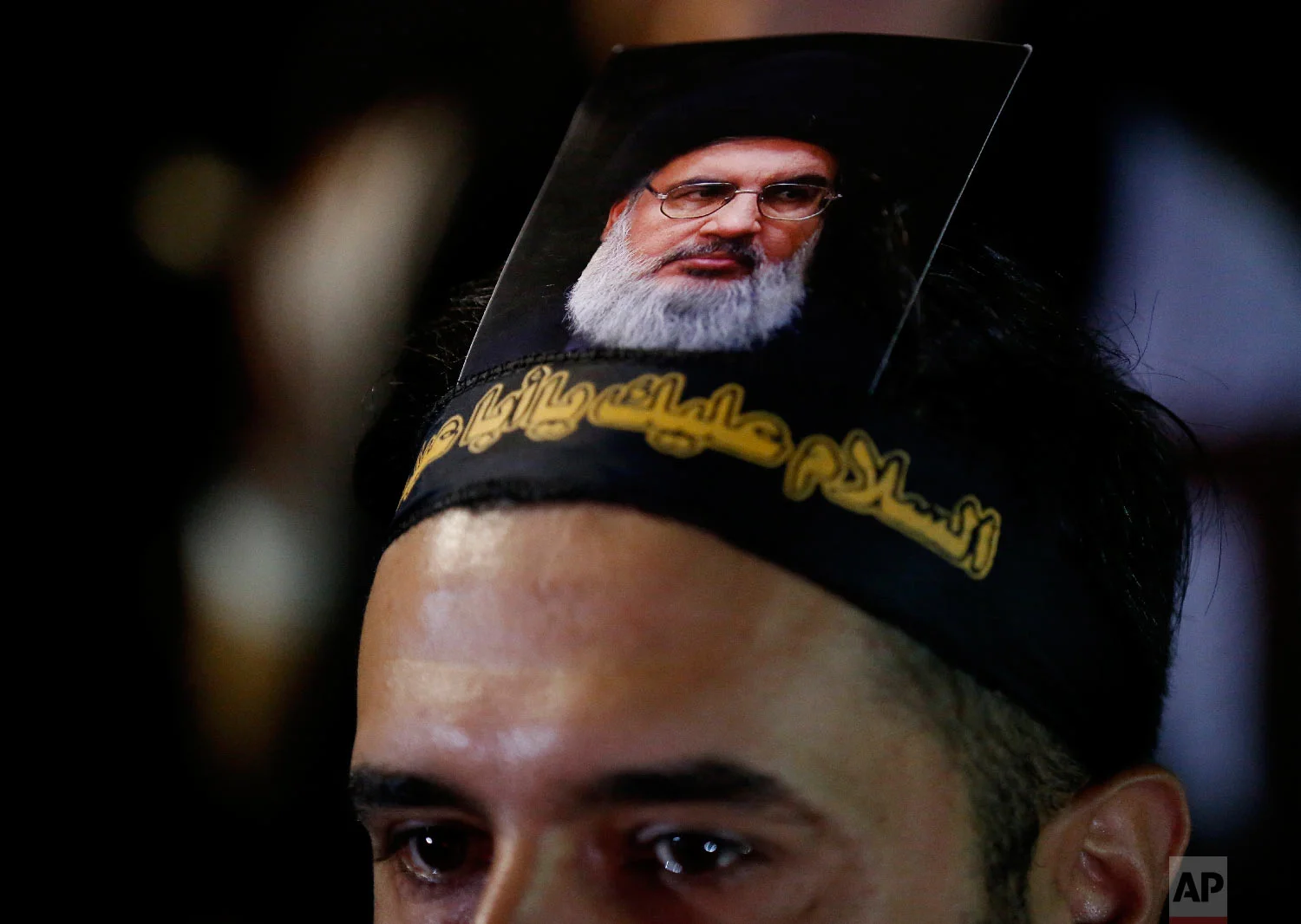 A Lebanese Shiite supporter of the Iranian-backed Hezbollah group, with a portrait on his head of Hezbollah leader Sheikh Hassan Nasrallah, attends an activities to mark the ninth of Ashura, a 10-day ritual commemorating the death of Imam Hussein, in a southern suburb of Beirut, Lebanon, Sept. 19, 2018. (AP Photo/Hussein Malla)