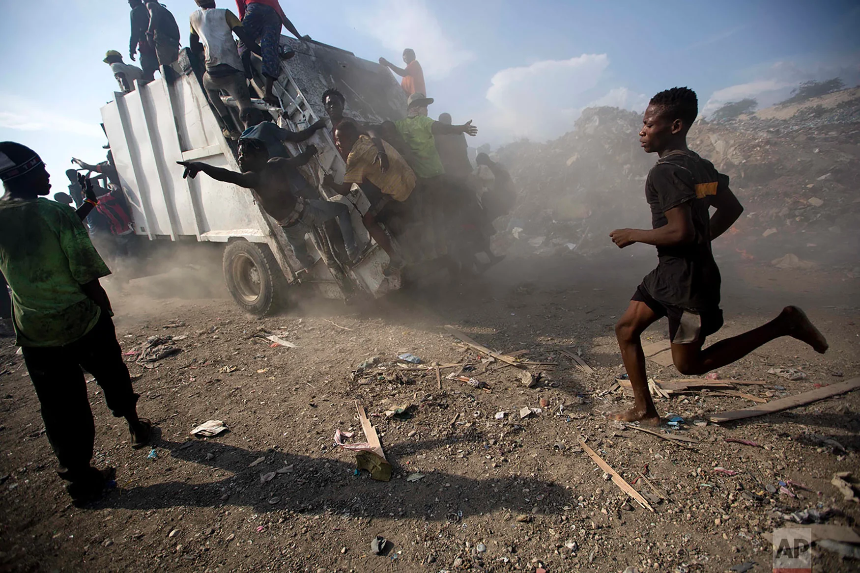 Scavengers climb on a trash truck arriving to unload at the Truitier landfill in the Cite Soleil slum of Port-au-Prince, Haiti, Aug. 28, 2018. Here in Cite Soleil, poisonous waste decomposes into the soil, seeping into nearby water sources and exacerbating dismal sanitary conditions. (AP Photo/Dieu Nalio Chery)