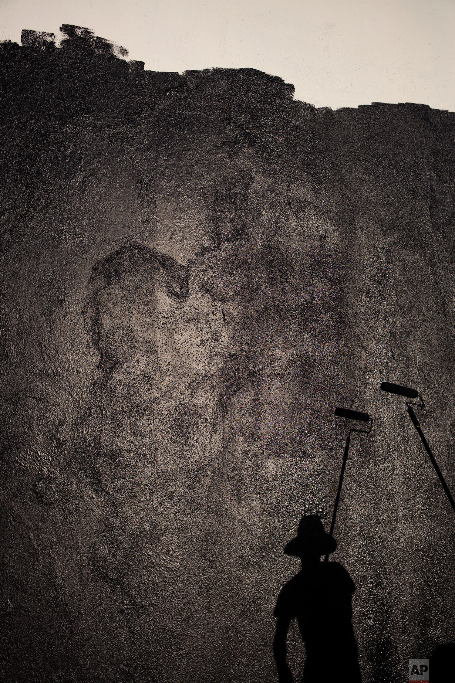 Artist's assistant Matthew Crumpton casts a shadow as he prepares a wall for a mural Monday, Oct. 8, 2018, in Los Angeles. (AP Photo/Jae C. Hong)