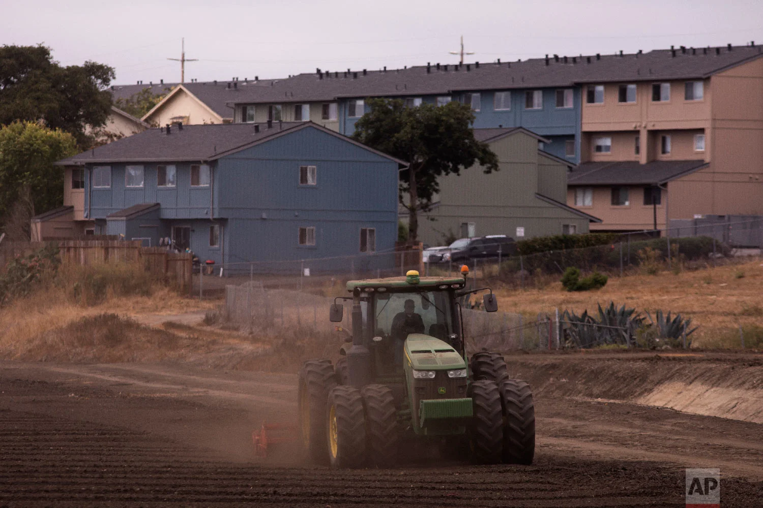 A tractor plows in a field near apartment buildings in Salinas, Calif., on Sept. 5, 2018. (AP Photo/Jae C. Hong)