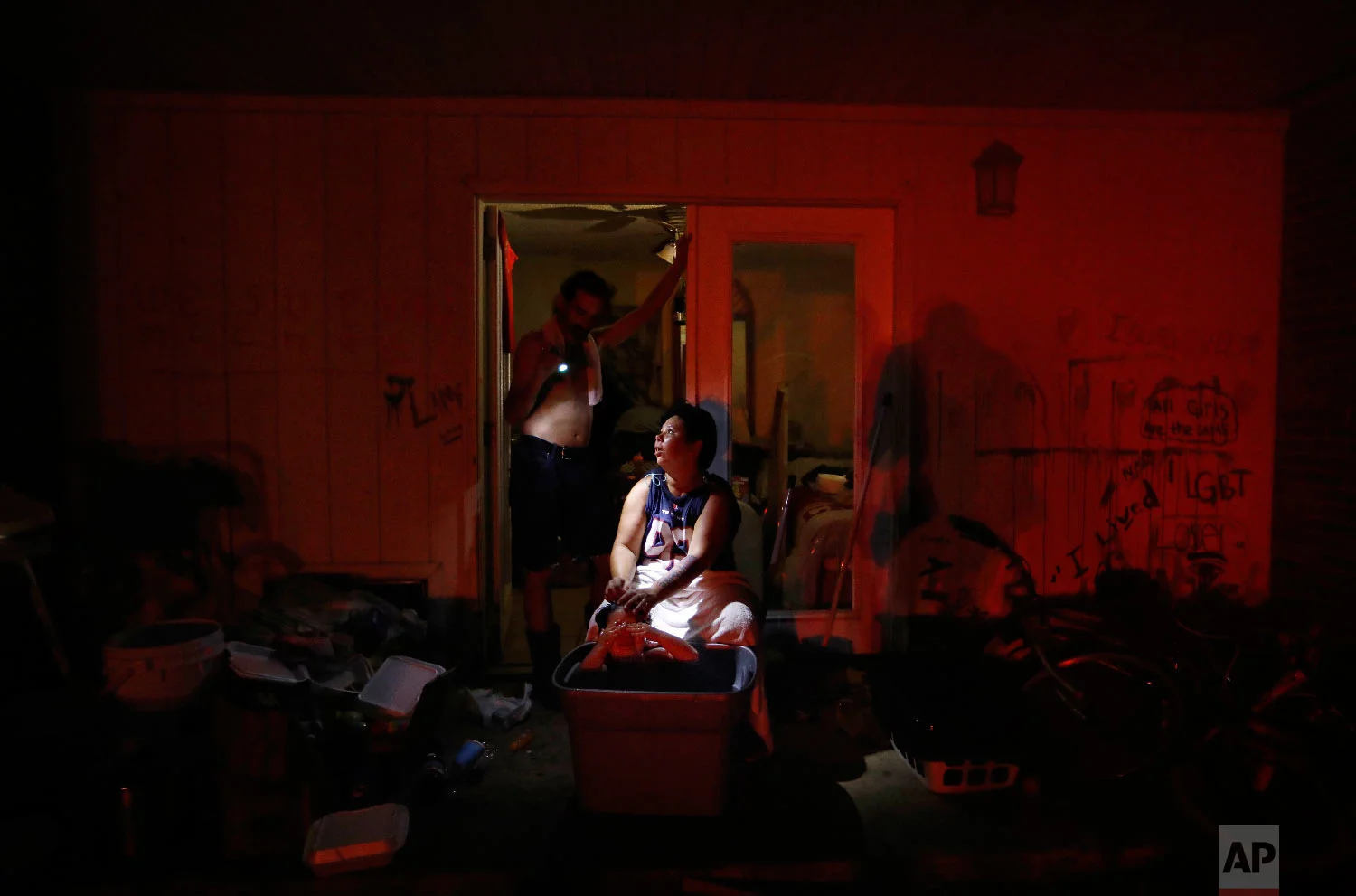 Tasha Hughes, bathes her daughter, Madison, 4, as Jeffrey Dumich holds a flashlight outside their room at the damaged American Quality Lodge where they continue to live without power in the aftermath of Hurricane Michael, in Panama City, Fla., Oct. 16, 2018. (AP Photo/David Goldman)