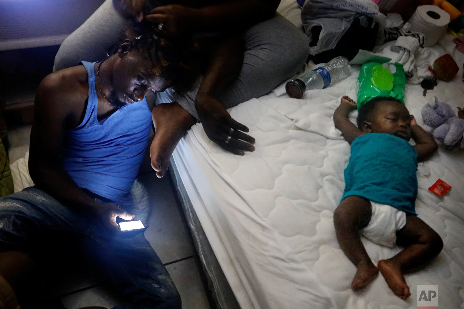Santional Morgan, has his hair braided by his wife Gabrielle as they sit by a lantern with their daughter Isabella, 3 months., in their room at the damaged American Quality Lodge where they continue to live without power in the aftermath of Hurricane Michael in Panama City, Fla., Oct. 16, 2018. (AP Photo/David Goldman)