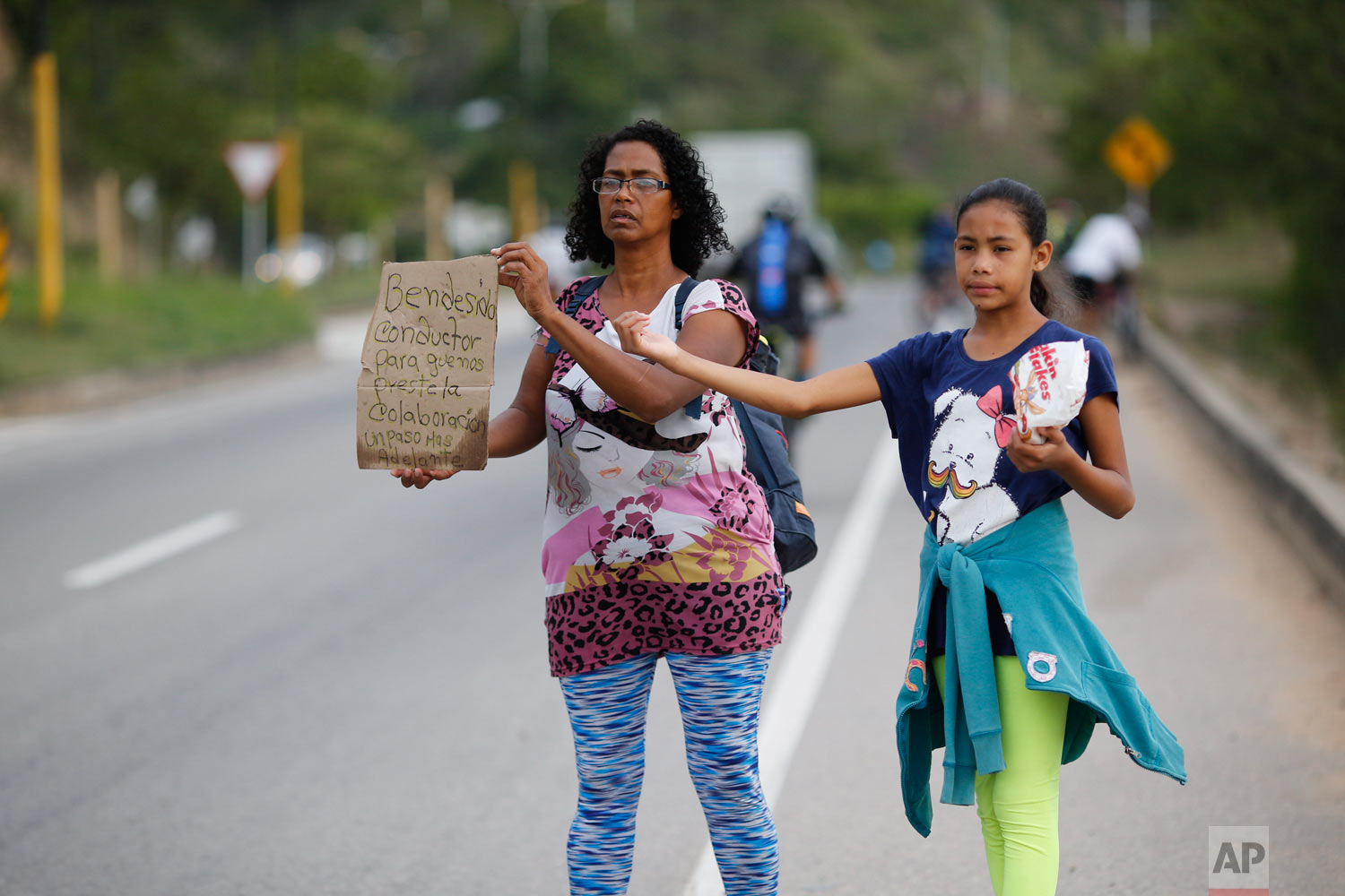 In this Sept. 2, 2018 photo, Venezuelan Sandra Cadiz holds up her handmade sign carrying the Spanish message: “Blessed driver, please help us with a ride,” as her 10-year-old daughter Angelis stands with her on the road leaving Giron, Colombia, as t