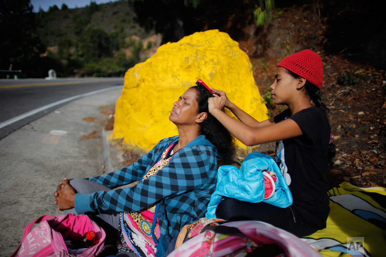  In this Sept. 1, 2018 photo, 10-year-old Venezuelan Angelis combs the hair of her mother Sandra Cadiz as they take a break from walking to the Berlin paramo, which leads to the city of Bucaramanga, Colombia, on their journey to Peru. The daughter of