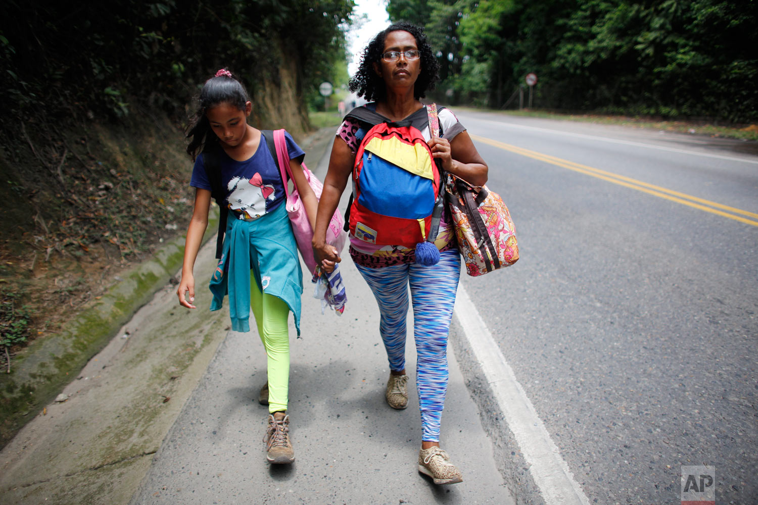 In this Sept. 2, 2018 photo, Venezuelan Sandra Cadiz holds the hand of her 10-year-old daughter Angelis as they walk on the shoulder of the road during their journey to Peru, near Dagota, Colombia. When Sandra Cadiz began struggling to feed her daug
