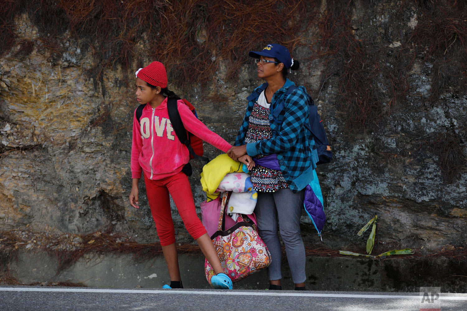  In this Sept. 1, 2018 photo, Venezuelan Sandra Cadiz holds the hand of her 10-year-old daughter, who's scared of the trucks racing by, as they wait for an opportunity to cross a highway on their way to the Berlin paramo, which leads to the city of B