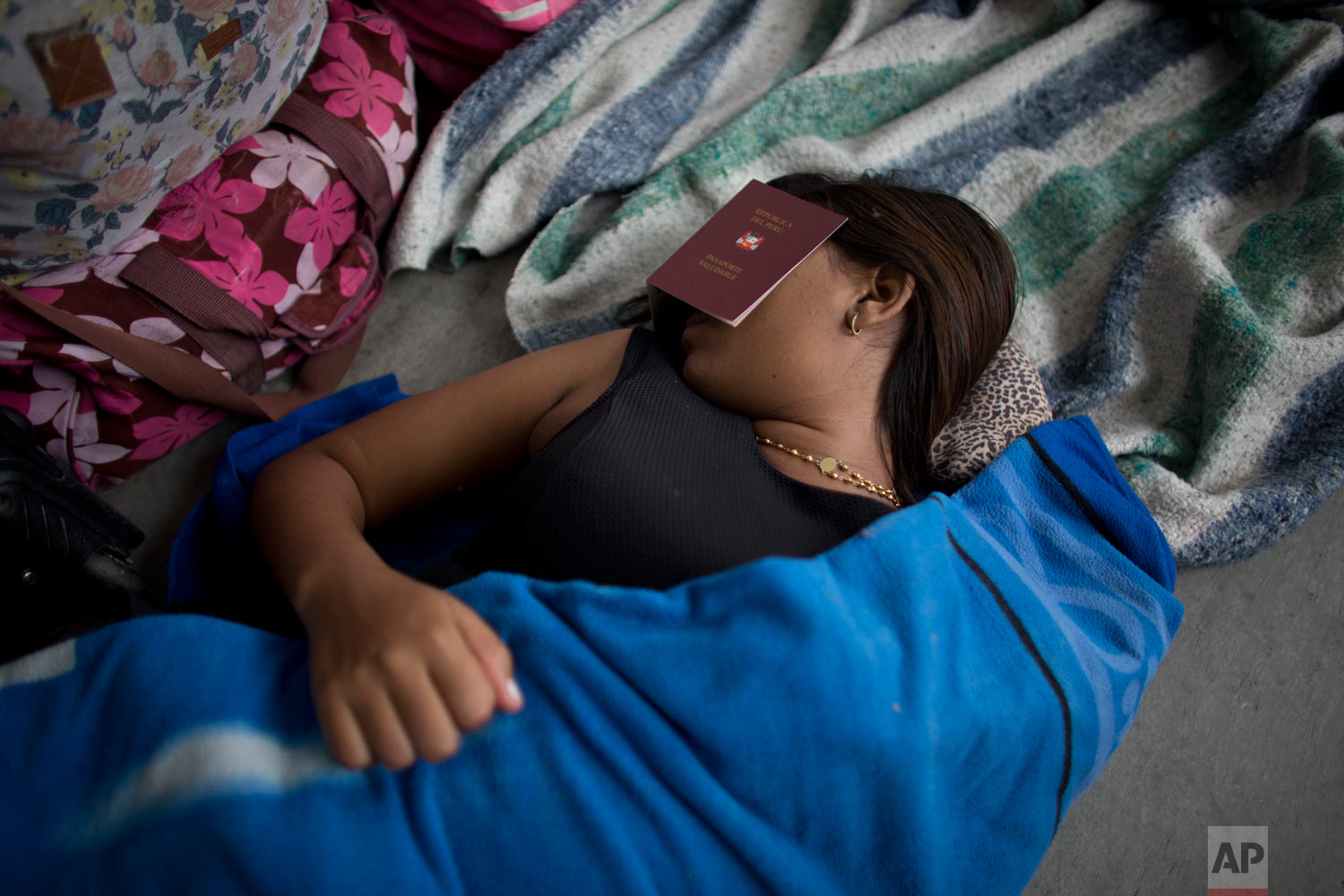  In this Sept. 7, 2018 photo, a Venezuelan woman covers her eyes with a Peruvian "health" passport to get some sleep near the Peruvian immigration office in Tumbes, Peru. At the border, Peruvian immigration authorities give foreigners a "Health Passp