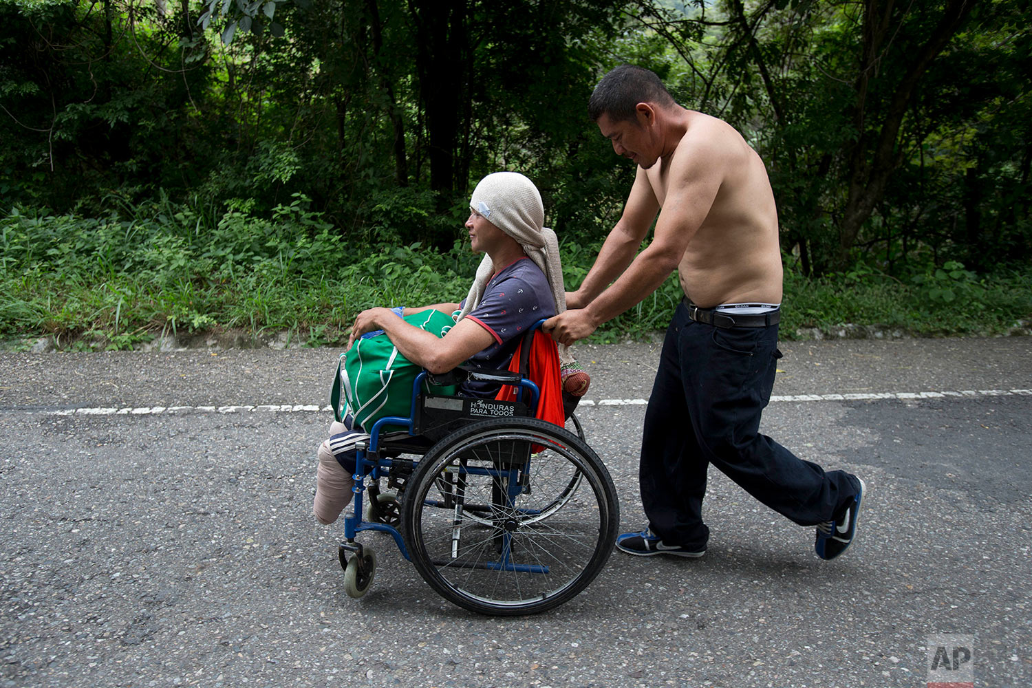  Honduran migrant Omar Orella pushes fellow migrant Nery Maldonado Tejeda in a wheelchair, as they travel with hundreds of other Honduran migrants making their way the U.S., near Chiquimula, Guatemala, Tuesday, Oct. 16, 2018. (AP Photo/Moises Castill