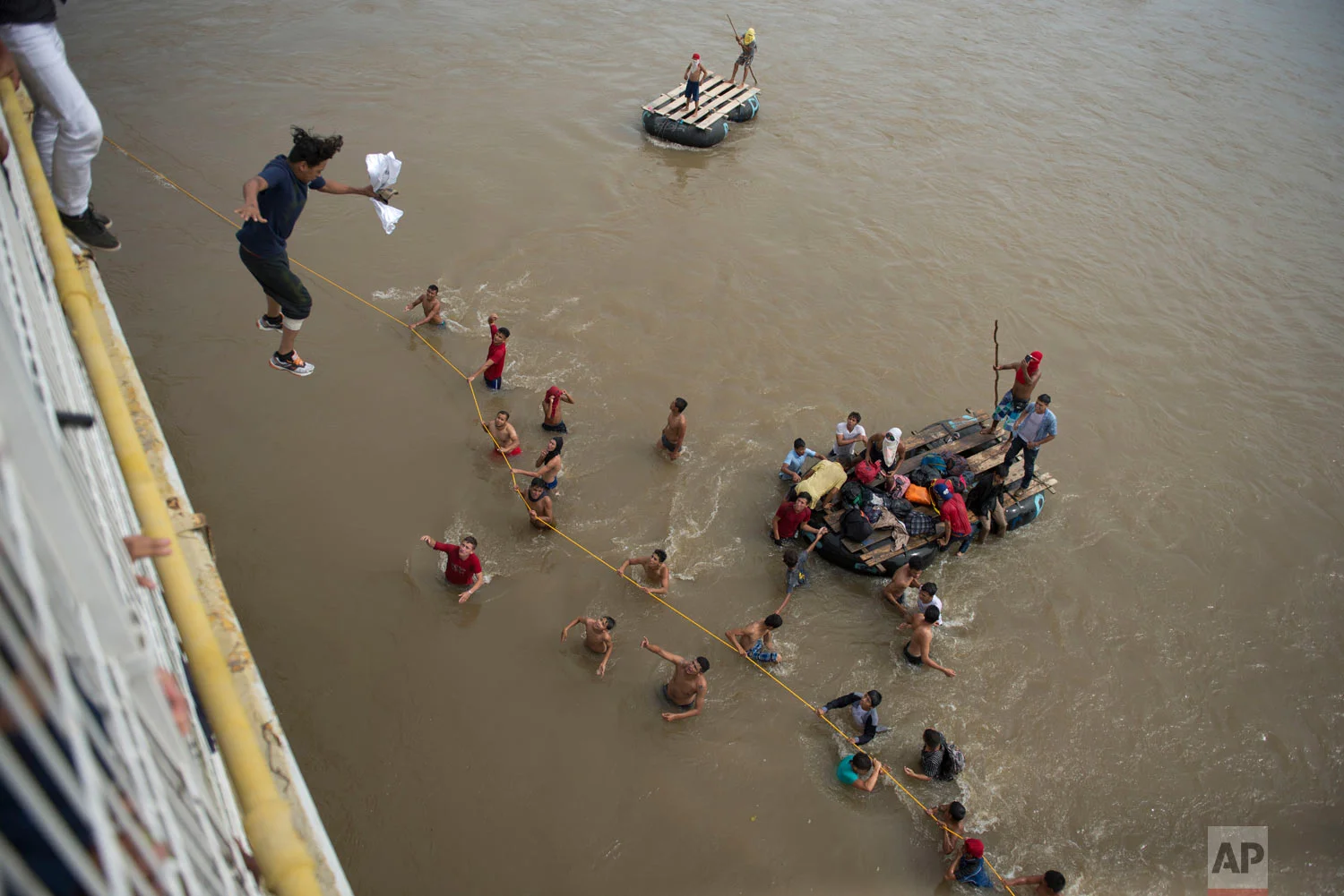 Migrants tired of waiting to cross into Mexico jump from a border bridge into the Suchiate River in Tecun Uman, Guatemala, Friday, Oct. 19, 2018, as a second caravan makes its way to the U.S. Some of the migrants traveling in a mass caravan towards the U.S.-Mexico border organized a rope brigade to ford its muddy waters. (AP Photo/Oliver de Ros)