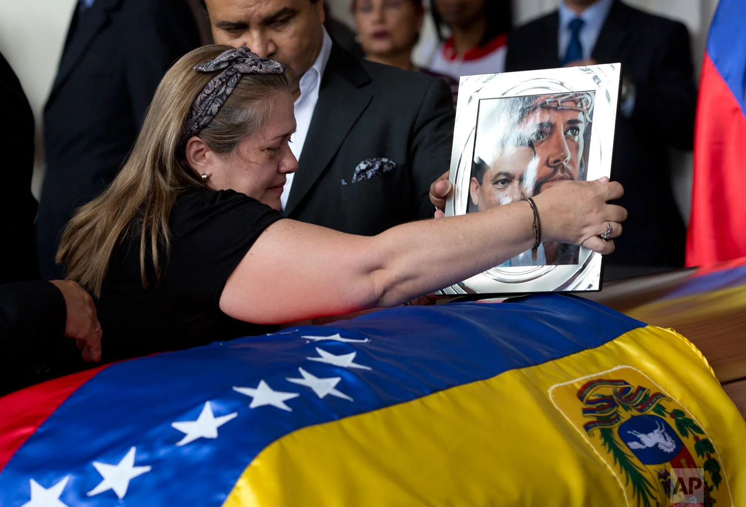 Luz Alban, the sister of opposition activist Fernando Alban places a portrait of her brother shadowed by an image of Jesus Christ, on his flag-draped casket during a ceremony at the National Assembly headquarters, in Caracas, Venezuela, Oct. 9, 2018. Questions and condemnation of Venezuela's leadership poured in following the suspicious death of Alban who authorities say evaded justice by throwing himself from the 10th floor of a police building. (AP Photo/Ariana Cubillos)