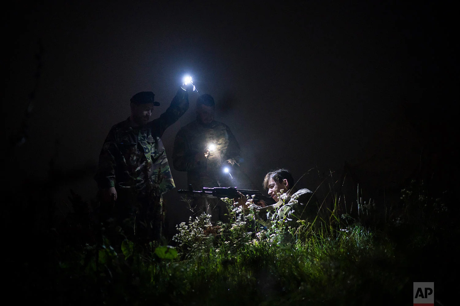 Yuri Chornota Cherkashin, head of Sokil, left, and instructor Georgiy Barylenko, center, point flashlights on a young participant of the "Temper of will" summer camp, organized by Svoboda party during a night drill on July 29, 2018, in a village near Ternopil, Ukraine. (AP Photo/Felipe Dana)