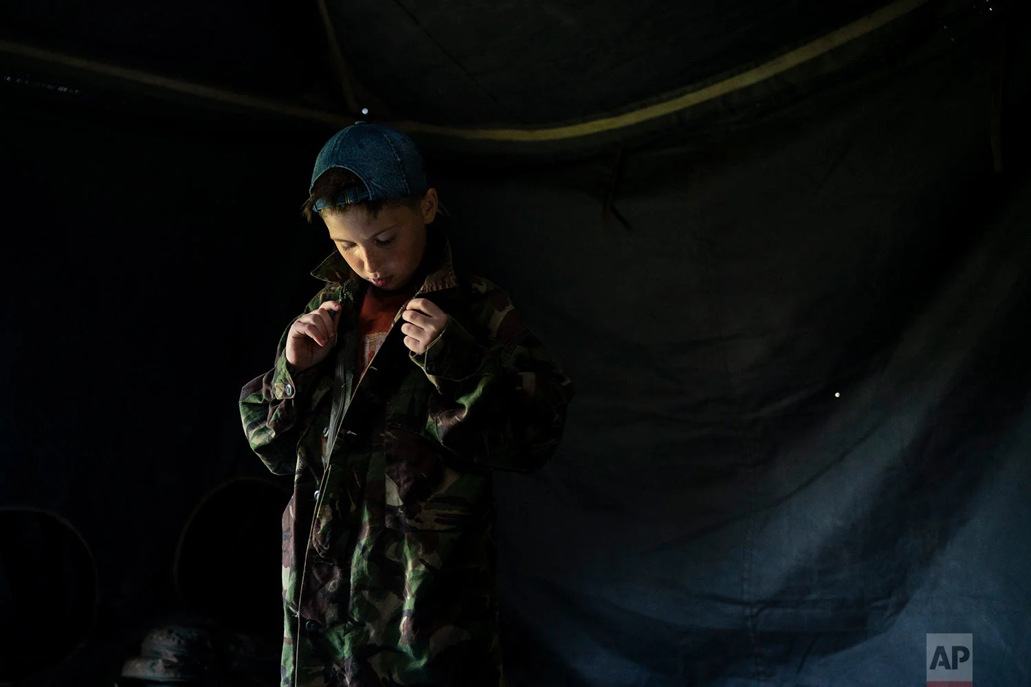 A young participant of the "Temper of will" summer camp, organized by the nationalist Svoboda party, buttons up a camouflage shirt as he prepares for an exercise on July 27, 2018, in a village near Ternopil, Ukraine. Campers as young as 8 years old practice using assault rifles. They are taught to shoot to kill Russians and their sympathizers. (AP Photo/Felipe Dana)
