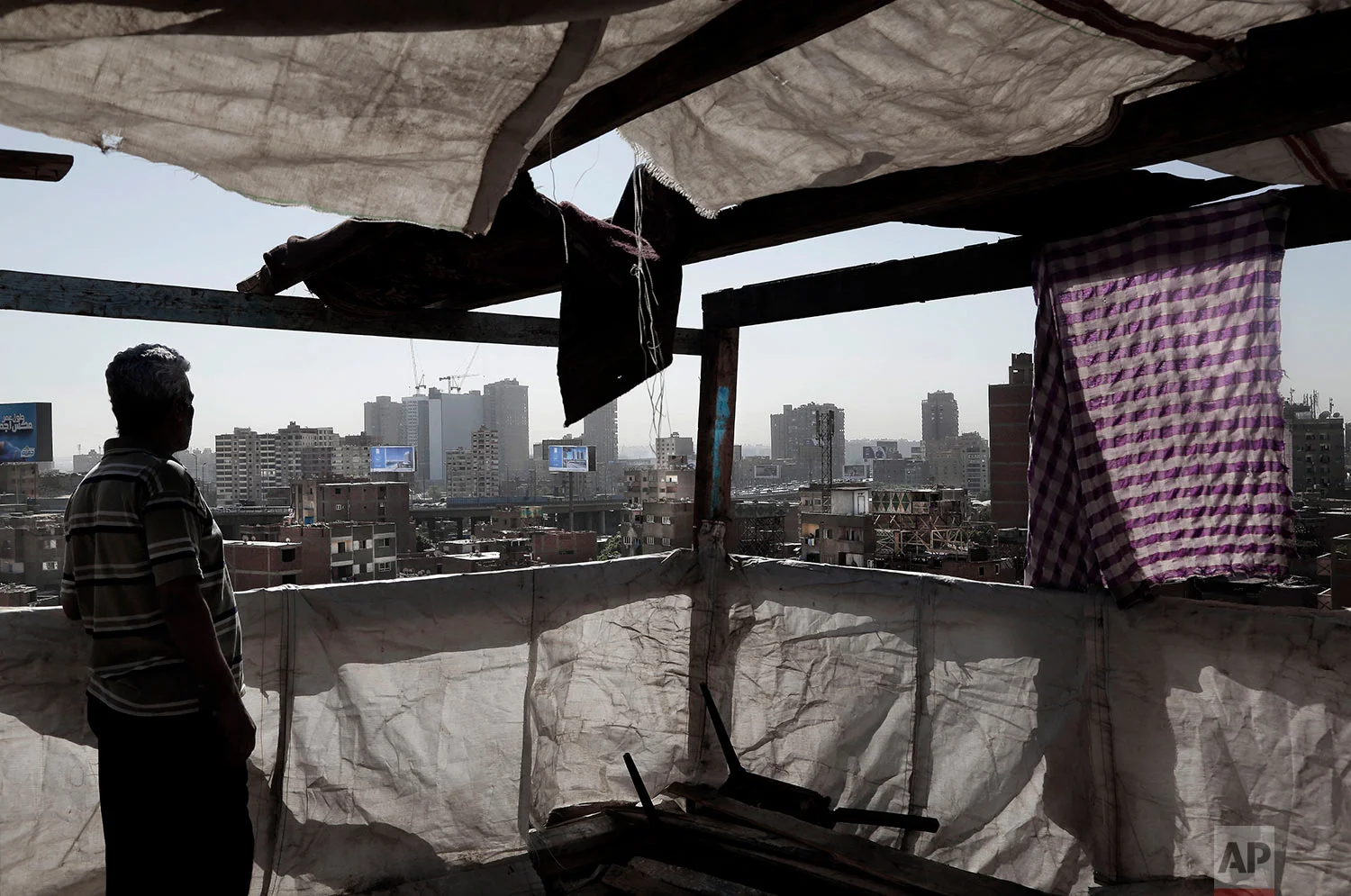 In this Oct. 28, 2018 photo, a man stands on the roof top of his home looking at the skyline littered with billboards promoting new residential suburban housing compounds, on the ring road, in Cairo, Egypt. (AP Photo/Nariman El-Mofty)