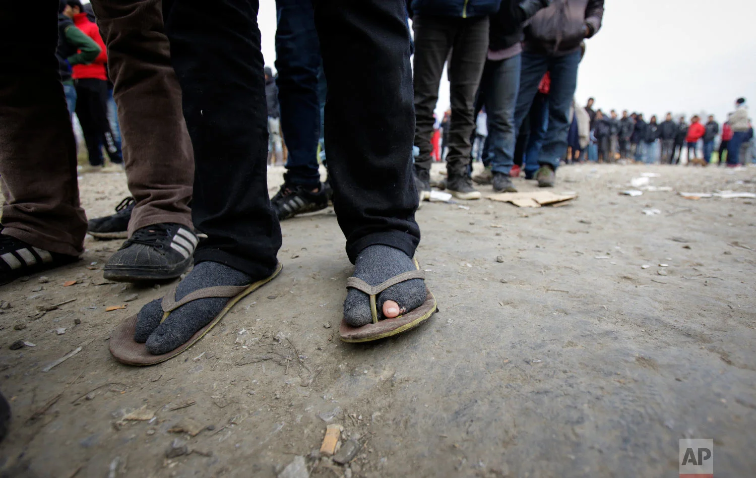 Migrants wearing tattered footwear wait in long lines for food distribution at a camp in Velika Kladusa, Bosnia, close to the border to Croatia, Sunday, Nov. 18, 2018. (AP Photo/Amel Emric)