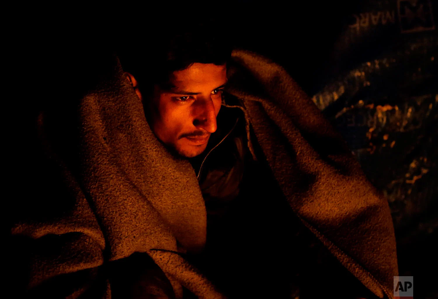 A migrant warms himself next to a fire at a camp in Velika Kladusa, Bosnia, close to the border to Croatia, Sunday, Nov. 18, 2018. (AP Photo/Amel Emric)