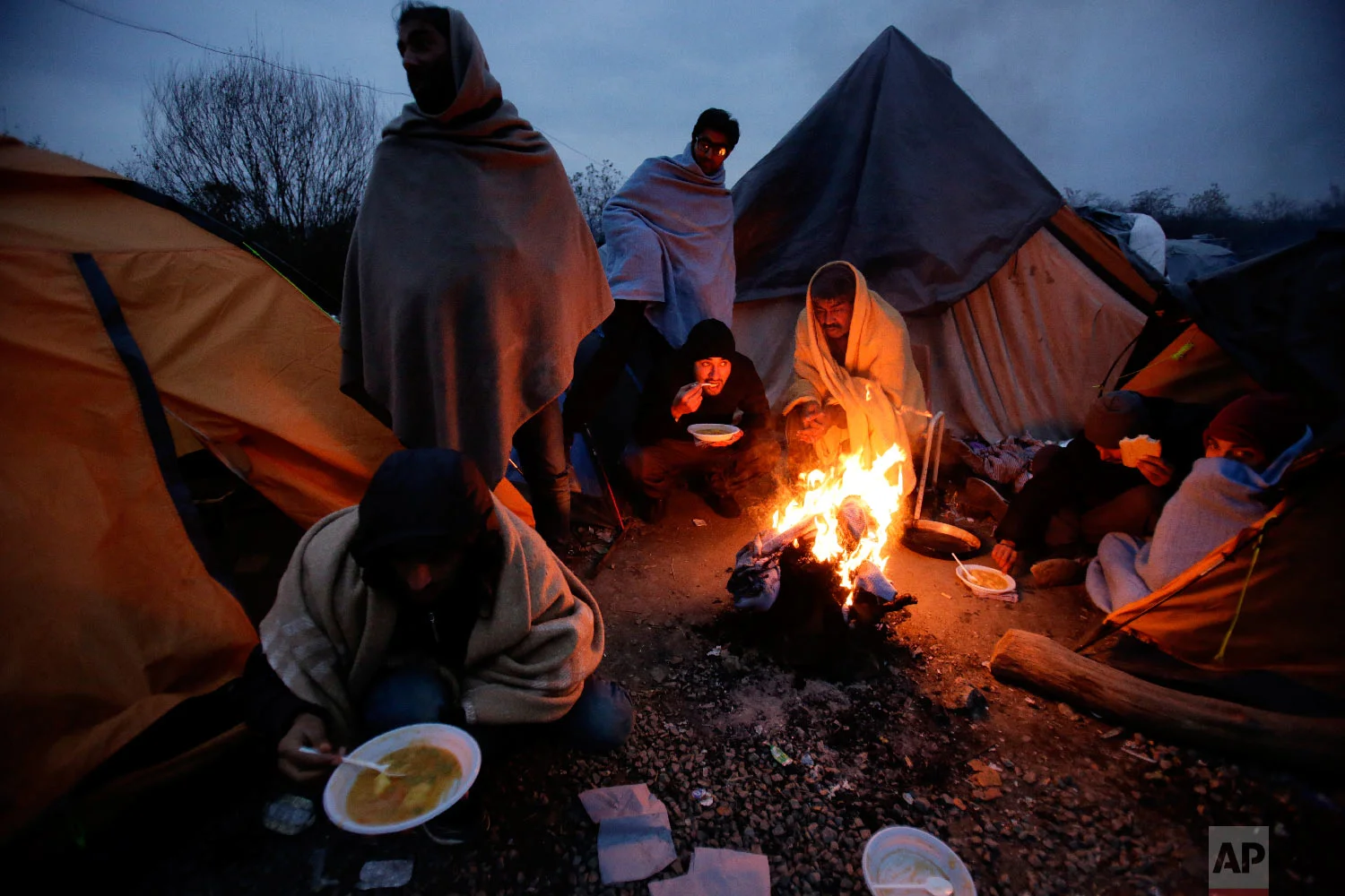Migrants eat around a fire at a camp in Velika Kladusa, Bosnia, close to the border to Croatia, Sunday, Nov. 18, 2018. (AP Photo/Amel Emric)