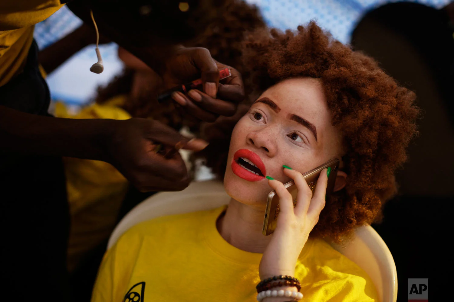 A contestant talks on her mobile phone while having her makeup done as she prepares to perform in the "Mr. & Miss Albinism East Africa" contest, organized by the Albinism Society of Kenya, in Nairobi, Kenya, Nov. 30, 2018. (AP Photo/Ben Curtis)