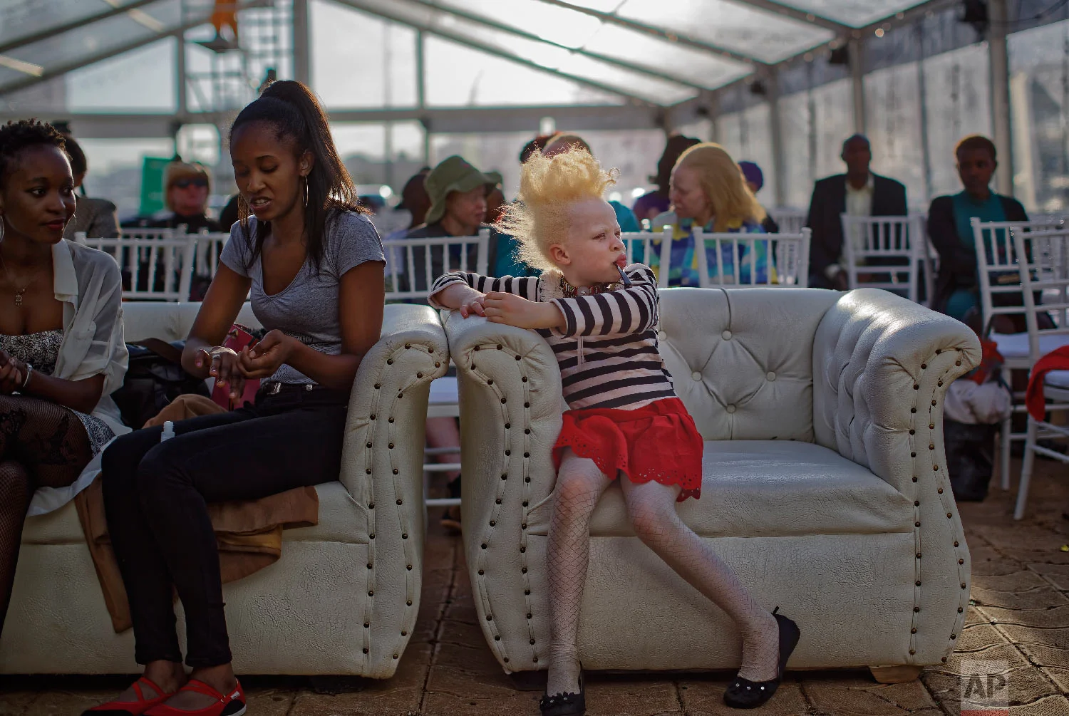 Albino girl Rebecca Zawadi, 8, right, sits next to Marion Jacklin, center-left, who helps train the contestants, as they wait for the start of the Mr. & Miss Albinism East Afric contest, organized by the Albinism Society of Kenya, in Nairobi, Kenya, Nov. 30, 2018. (AP Photo/Ben Curtis)