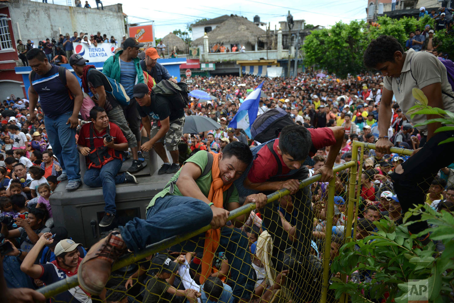  Young men climb over a fence in Tecun Uman, Guatemala, as thousands of Central American migrants rush across the border towards Mexico on Oct. 19, 2018. (AP Photo/Oliver de Ros) 