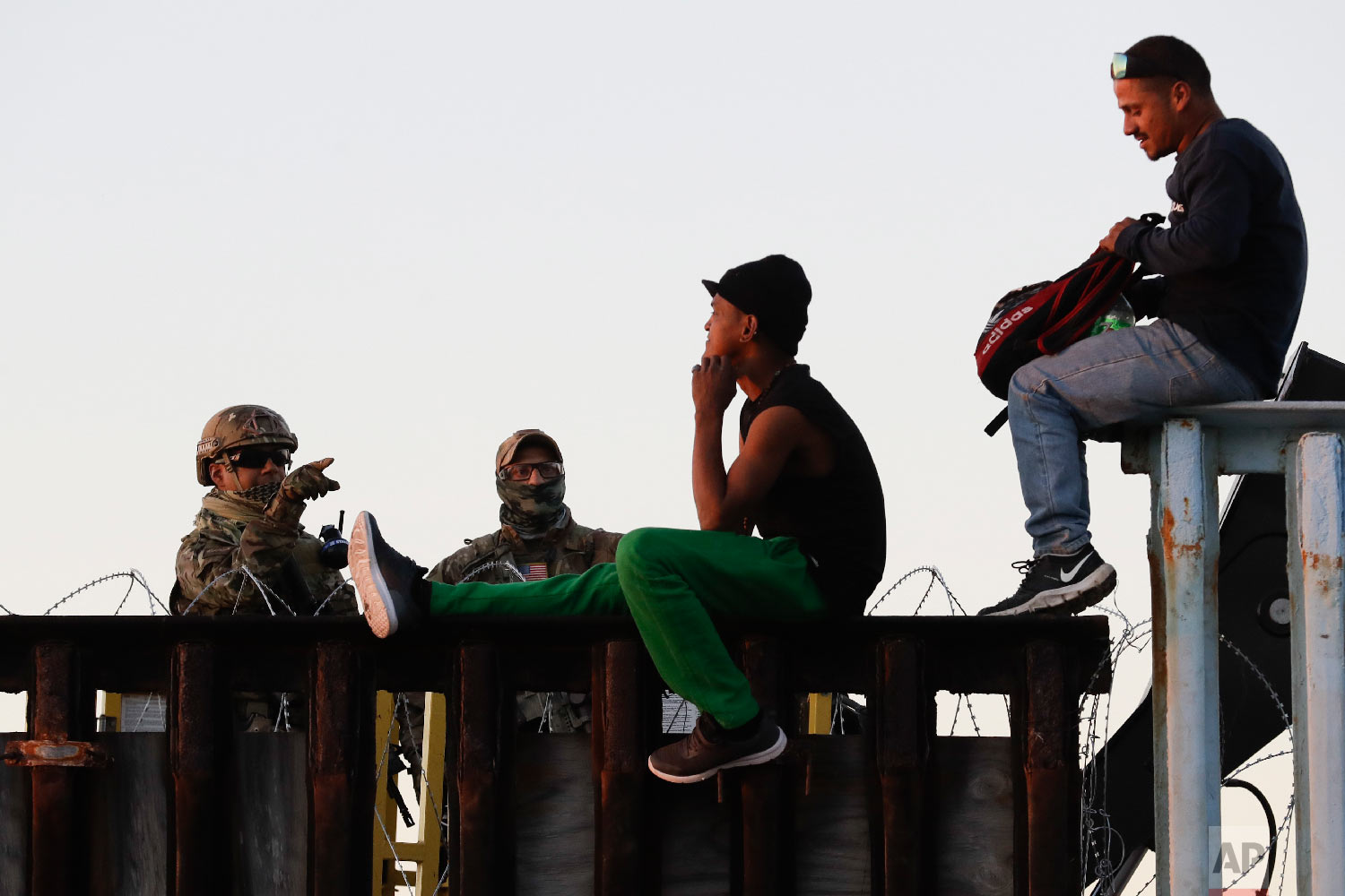 U.S. Border Patrol agents, left, speak with two Central American migrants as they sit atop the border structure separating Mexico and the United States in Tijuana, Mexico, on Nov. 14, 2018. (AP Photo/Gregory Bull) 