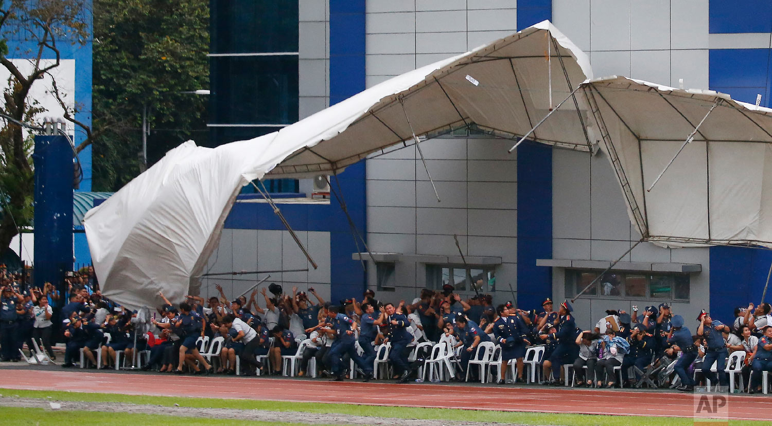  Philippine National Police officers and employees react as their tent is toppled by the downwash of a hovering police helicopter performing a salute during the 117th Philippine National Police Service anniversary at Camp Crame in Quezon City, a subu