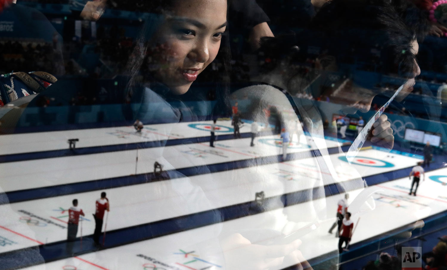  A woman's face is reflected in glass as she watches men's curling matches at the 2018 Winter Olympics in Gangneung, South Korea, on Feb. 18, 2018. (AP Photo/Natacha Pisarenko) 