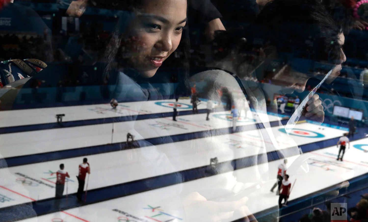 A woman's face is reflected in glass as she watches men's curling matches at the 2018 Winter Olympics in Gangneung, South Korea, on Feb. 18, 2018. (AP Photo/Natacha Pisarenko)