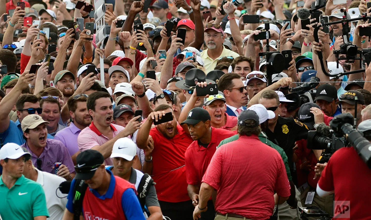 Tiger Woods, lower center, and Rory McIlroy, lower left, emerge from a horde of fans following Tiger on their way to the 18th green during the final round of the Tour Championship golf tournament in Atlanta on Sept. 23, 2018. (AP Photo/John Amis)